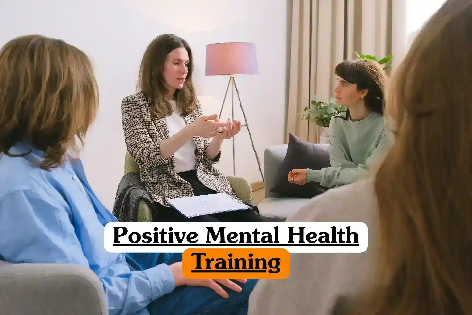 Positive Mental Health Training course banner with group of people sitting in comfortable indoor setting engaged in supportive discussion one person leading conversation gesturing with hands while others listen attentively background with lamp plant and curtains professional mental health education environment.