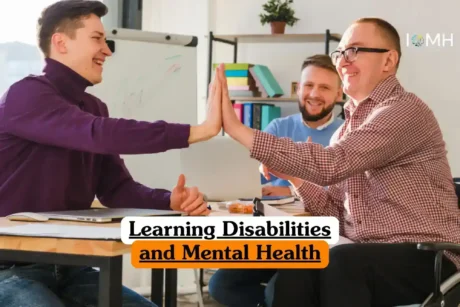 Learning Disabilities and Mental Health course banner with three individuals in bright office classroom two giving high five at desk with laptops papers and whiteboard with colorful marker lines while third smiles in background shelves with books folders.