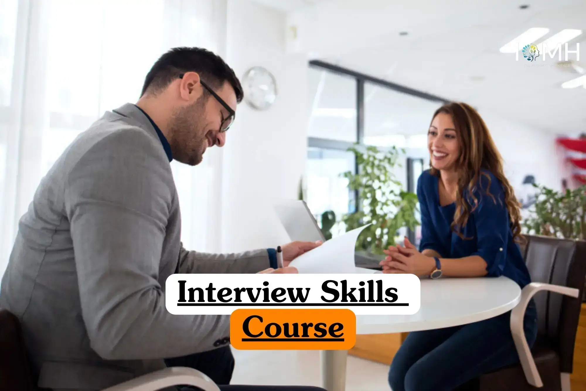 Interview Skills Course banner with professional conducting interview at round table in modern office with papers plants and clock on wall.