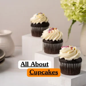 Theoretical food science and pastry arts training banner featuring three chocolate cupcakes with white swirl frosting and colorful sprinkles, elegantly arranged on white marble-textured blocks.
