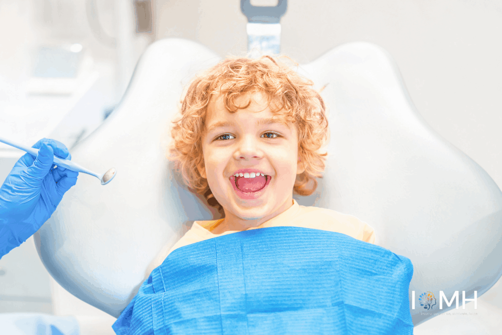 Happy young child smiling during a dental checkup with an oral health practitioner holding a dental mirror