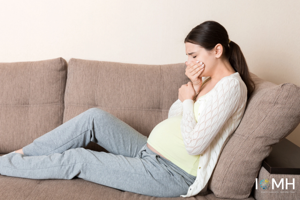Pregnant woman experiencing morning sickness and nausea while resting on a sofa at home