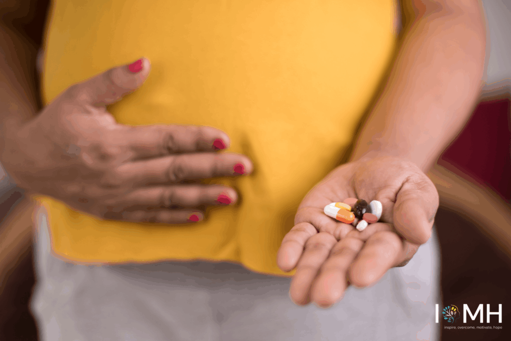 Pregnant woman in yellow top holding her baby bump with one hand while offering a selection of prenatal vitamins and medication pills in the other – safe pregnancy supplements guidance