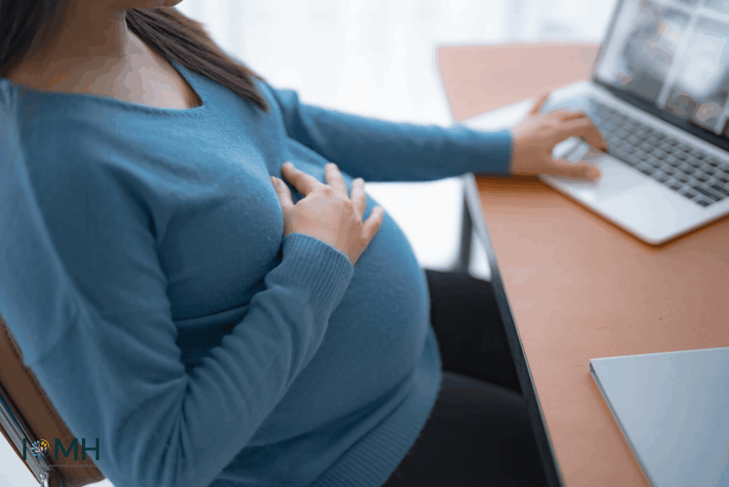 Pregnant woman working at a desk while supporting her baby bump during pregnancy.