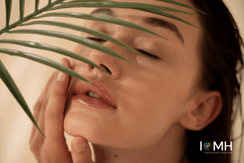 Woman with glowing natural skin gently touching her face, partially covered by green palm leaves for a natural skincare look